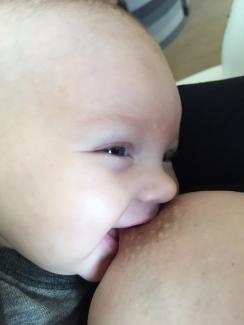 Smilende baby ved brystet
